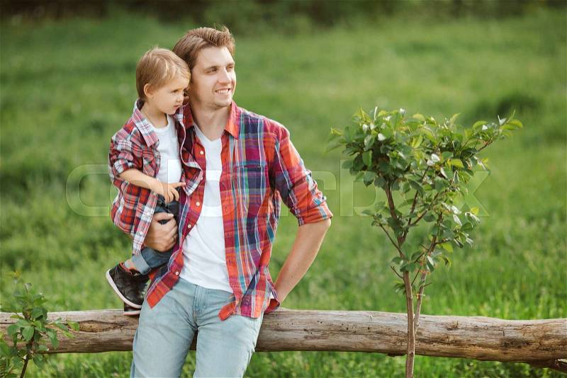Portrait of a father holding his son and sitting on fence , rural look, outdoors, stock photo
