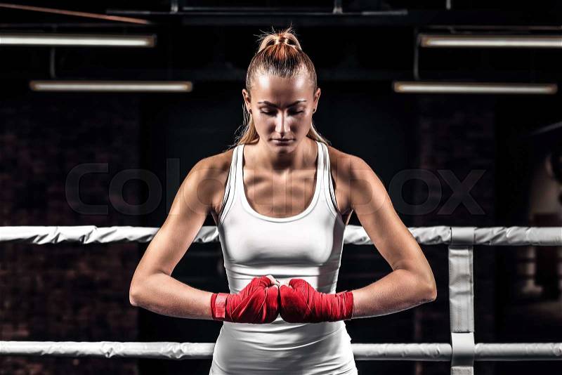 Young athlete woman showing her fists with bandage ready for fight eyes closed. Close up boxer female on uniform stands in the ring and getting ready to box, stock photo