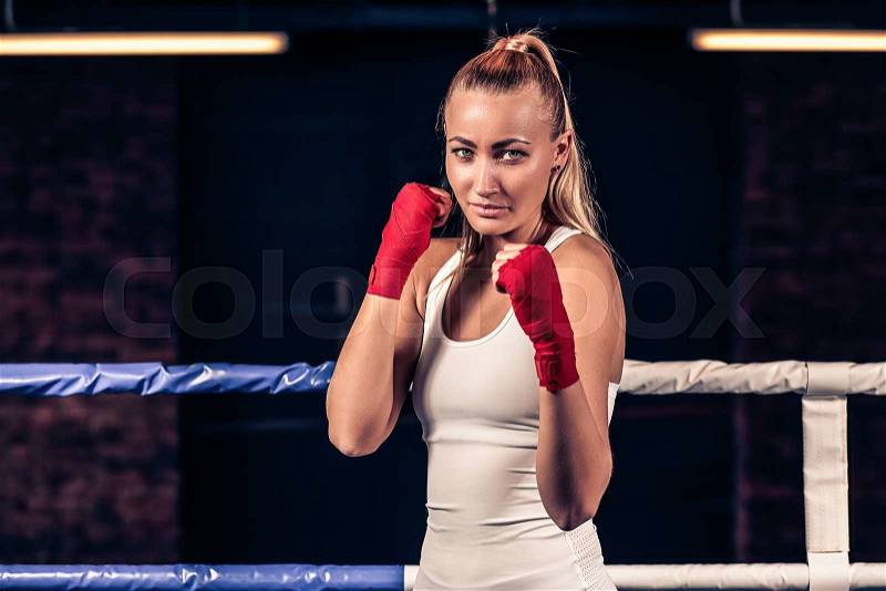 Portrait of young beautiful boxer woman ready to kick with red boxing bandage on hands in gym. Strong hand and fist, ready for fight and active exercise, stock photo