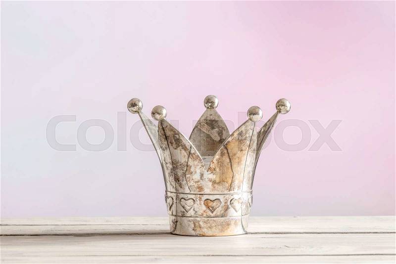 Royal crown on a wooden table on a pink background, stock photo