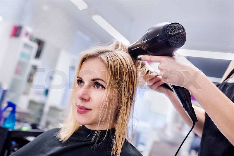 Hands of unrecognizable professional hairdresser drying hair of her client, new haircut, blonde female customer, stock photo
