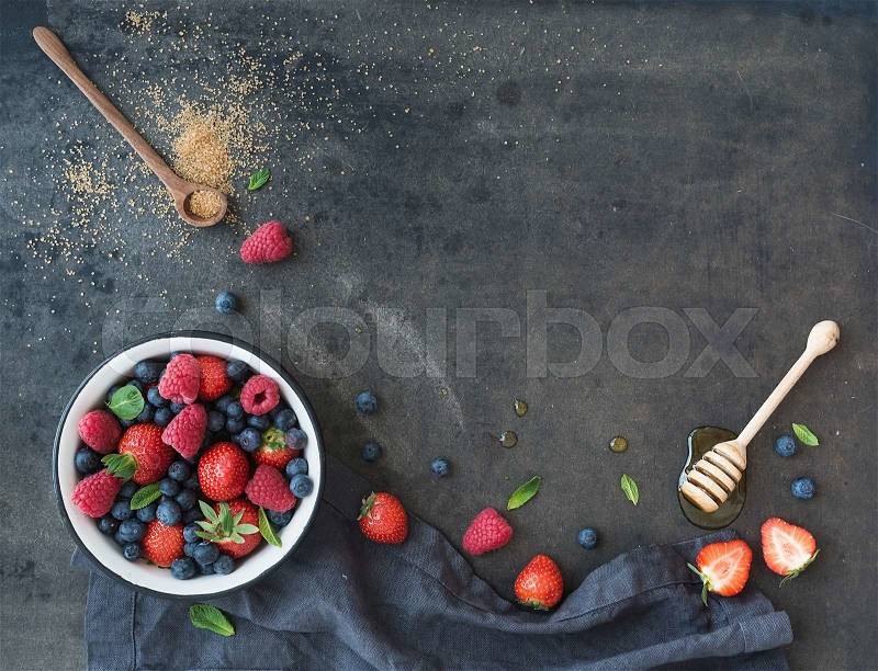 Berry frame with copy space on right. Strawberries, raspberries, blueberries and mint leaves, honey, cane sugar, dark grunge background, top view, copy space, stock photo