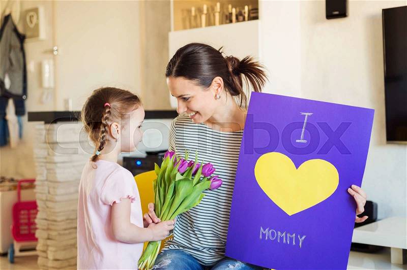 Mothers day, cute little girl giving flowers and greeting card to her mum, stock photo