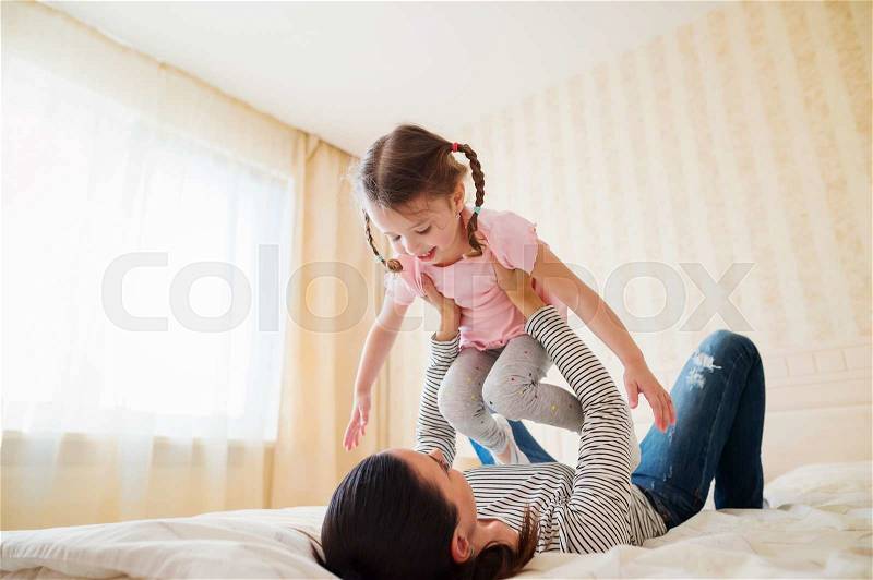 Beautiful young mother having fun with her daughter on bed in her bedroom, stock photo