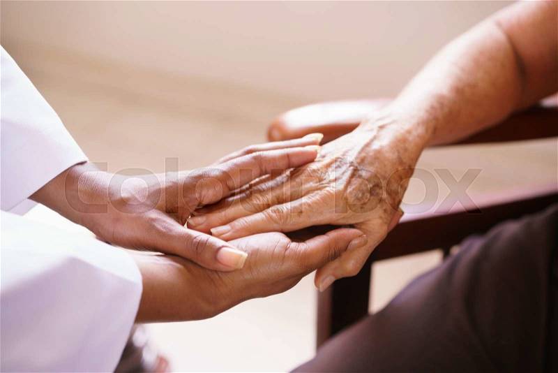 Old people in geriatric hospice: Aged patient receives the visit of a female black doctor. They shake their hands and talk in the hospital, stock photo