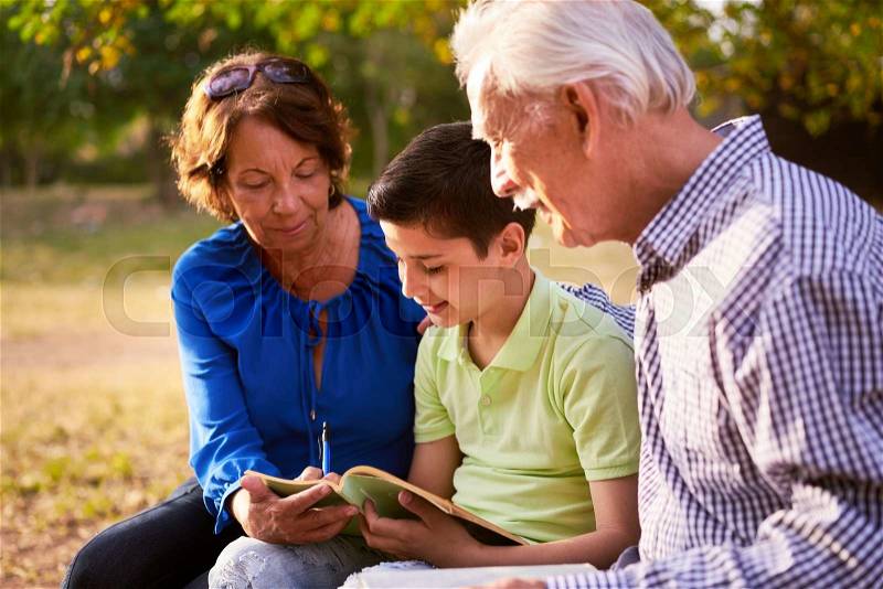 Grandparents educating grandson: Senior woman and old man spending time with their grandchild in park. The old people help the preteen kid studying and doing his school homework, stock photo