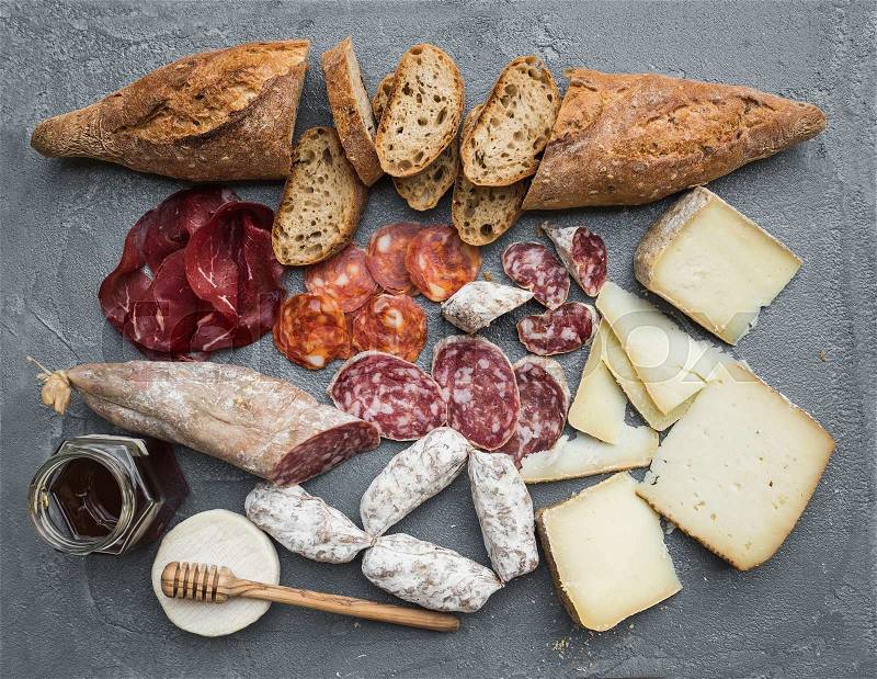 Cheese and meat appetizer selection or wine snack set. Variety of italian cheese, salami, bresaola, baguette and honey on over grey concrete backdrop, top view, stock photo