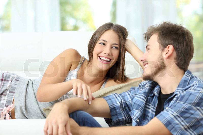 Happy marriage or couple flirting and laughing lying on a couch at home, stock photo