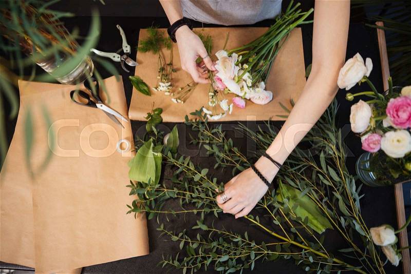 Top view of hands of young woman florist creating bouquet of flowers on black table, stock photo
