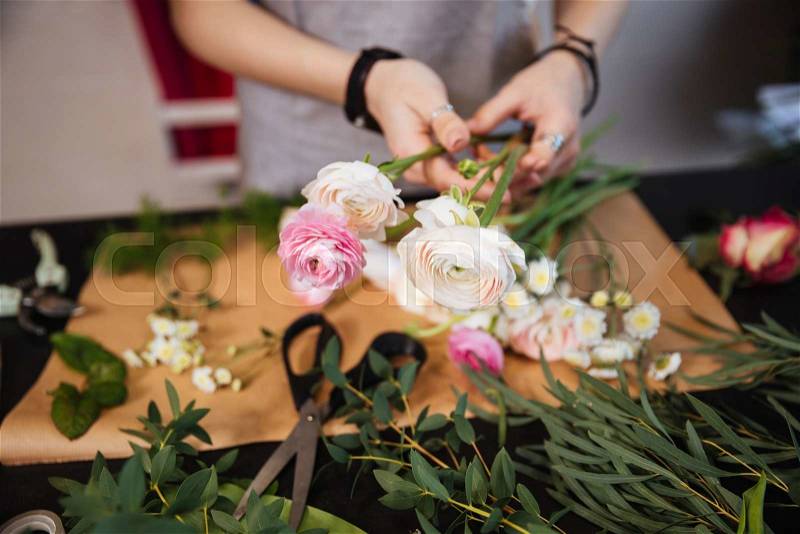 Coseup of hands of young woman florist creating bouquet of pink roses on the table, stock photo