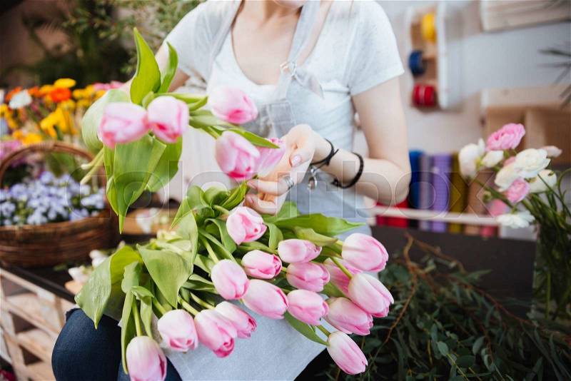 Closeup of young woman florist sitting and taking car eof pink tulips in flower shop, stock photo