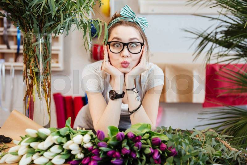 Portrait of charming amusing young woman florist making funny face standing in flower shop, stock photo
