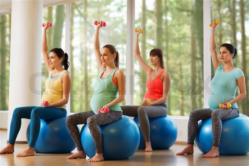 Pregnancy, sport, fitness, people and healthy lifestyle concept - group of happy pregnant women with dumbbells exercising on ball in gym, stock photo