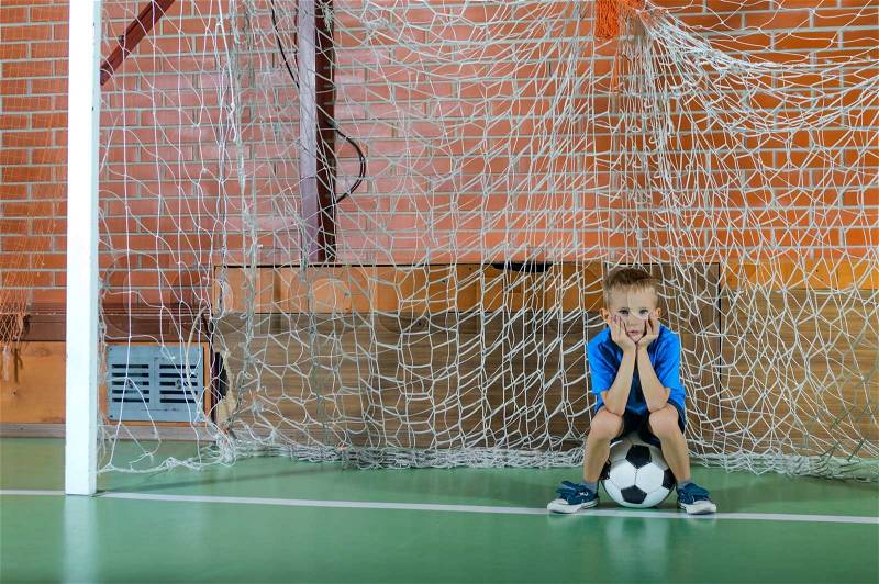 Young boy playing goalie holding a soccer ball as he stands in the goals on an indoor court preparing to throw the ball, stock photo
