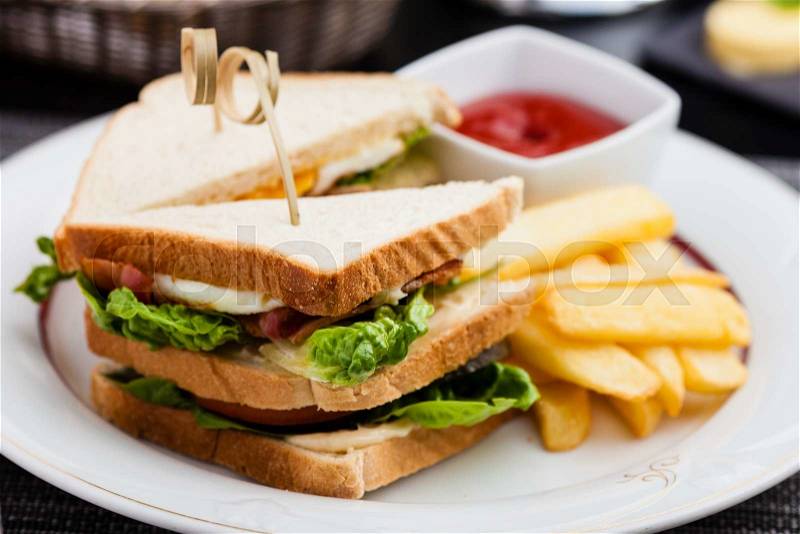 Sandwich with fried eggs, bacon and lettuce served with french fries and ketchup, stock photo