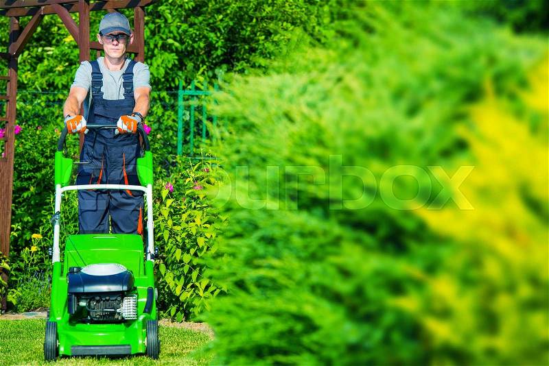 Caucasian Gardener Mowing the Grass Using Professional Grass Mower. Garden Works, stock photo