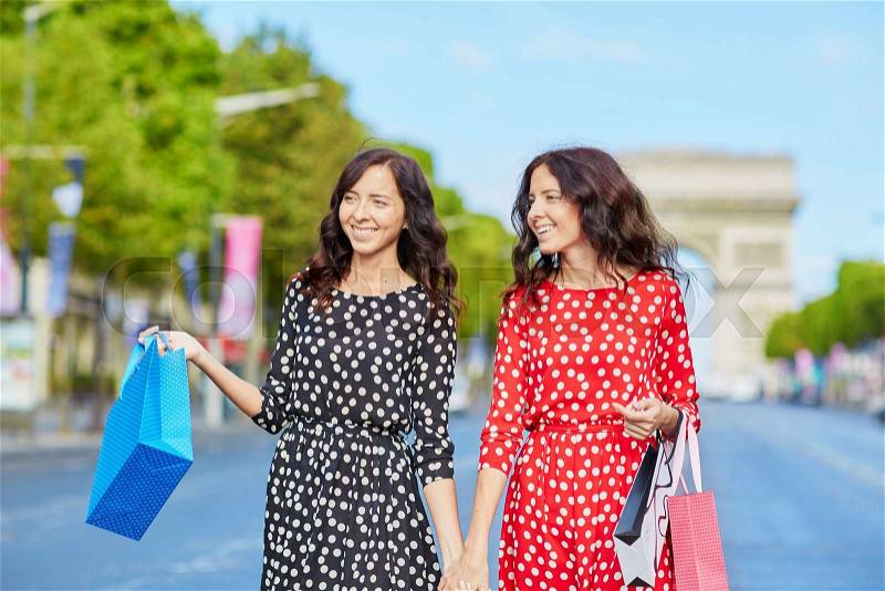 Happy twin sisters doing shopping on holidays in France, walking with shopping bags in front of Arc de Triomphe on Champs-Elysees, Paris, France, stock photo