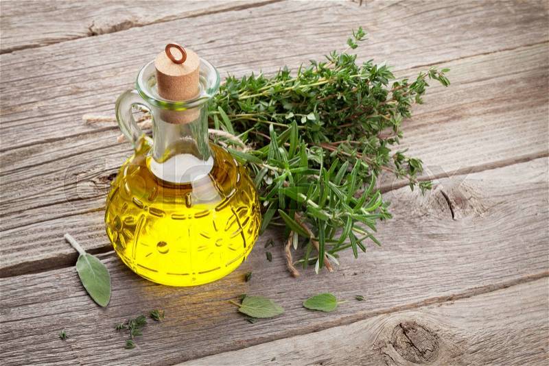Olive oil and fresh garden herbs on wooden table, stock photo
