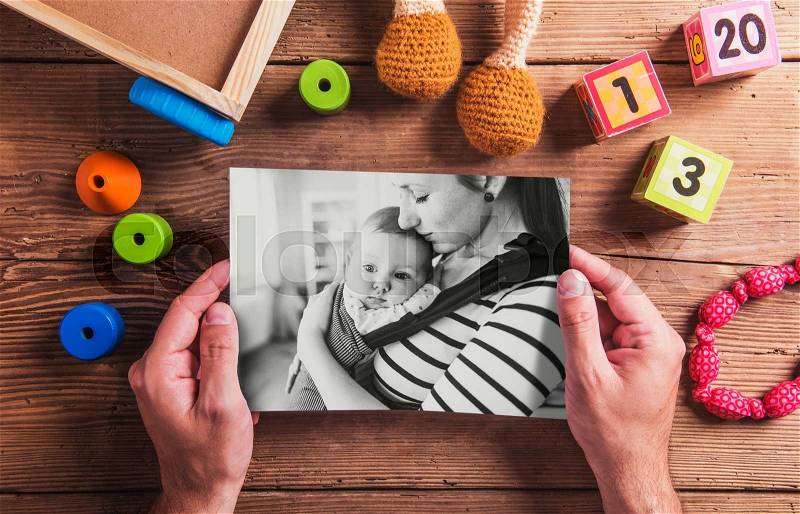 Mothers day composition. Unrecognizable man holding black-and-white picture. Various toys. Studio shot on wooden background, stock photo