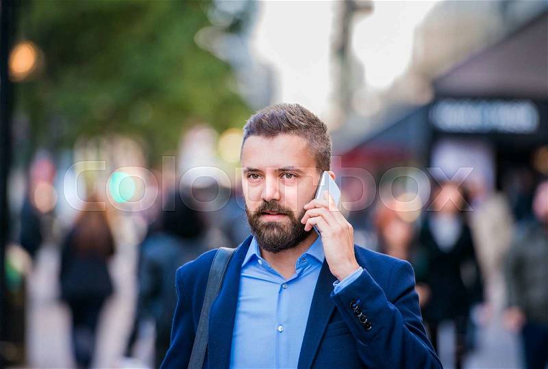 Hipster manager holding a smart phone, making a phone call, walking in the street of London, stock photo