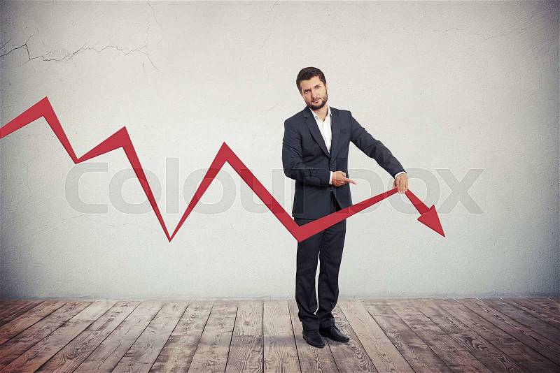 Disappointed businessman pointing to red graph arrow down, stock photo