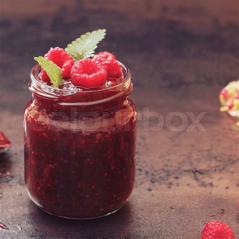 Raspberry jam, close up. A jar of raspberry jam and fresh raspberries on top. Macro, selective focus, vintage toned image, blank space, stock photo