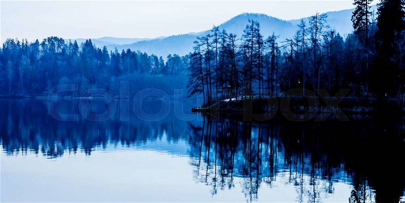 Dark blue lake shore with forest and reflection in surface, stock photo