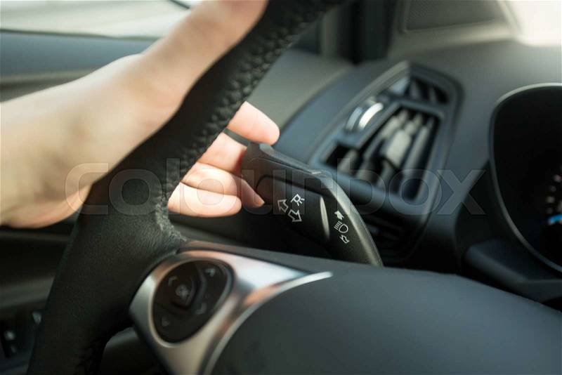 Closeup photo of woman driving car and using turn signal switch, stock photo