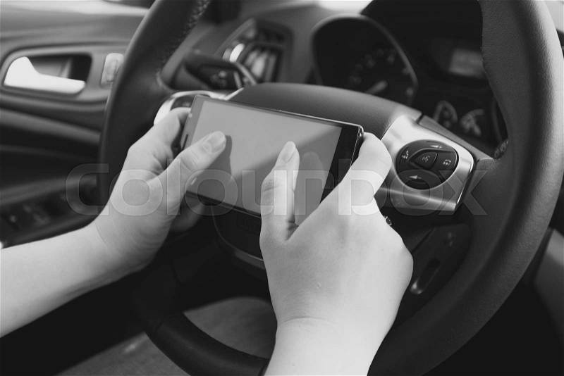 Closeup black and white photo of driver typing message while driving a car, stock photo