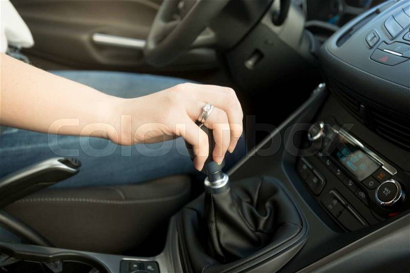 Closeup photo of young woman shifting gearbox in car, stock photo