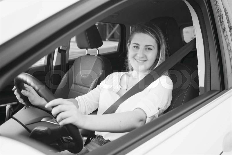 Black and white portrait of smiling woman driving car and looking at camera, stock photo