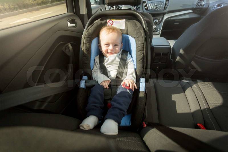 Happy smiling baby boy posing in child safety car seat, stock photo