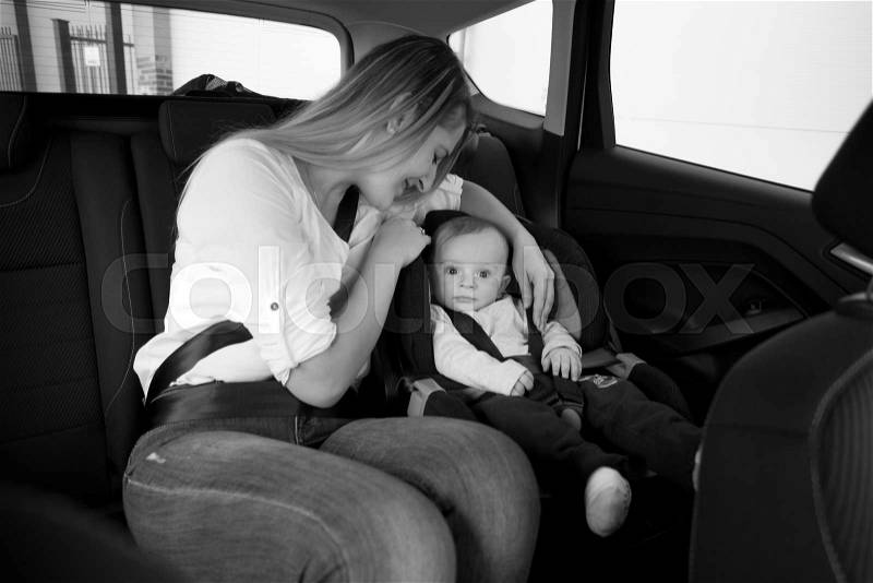 Black and white photo of smiling mother sitting on car backseat with her baby, stock photo