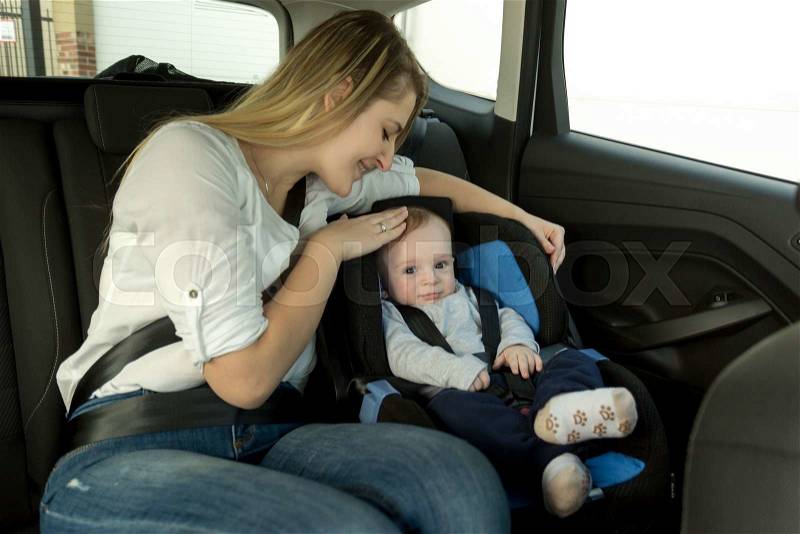 Portrait of young caring mother with her baby boy on car back seat, stock photo