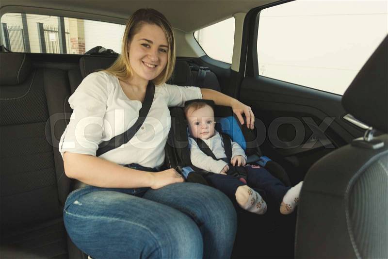Portrait of smiling young mother and baby boy in car safety seat, stock photo