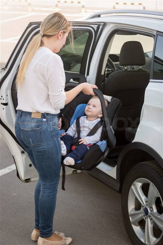 Young mother putting car seat with her baby boy in the car, stock photo