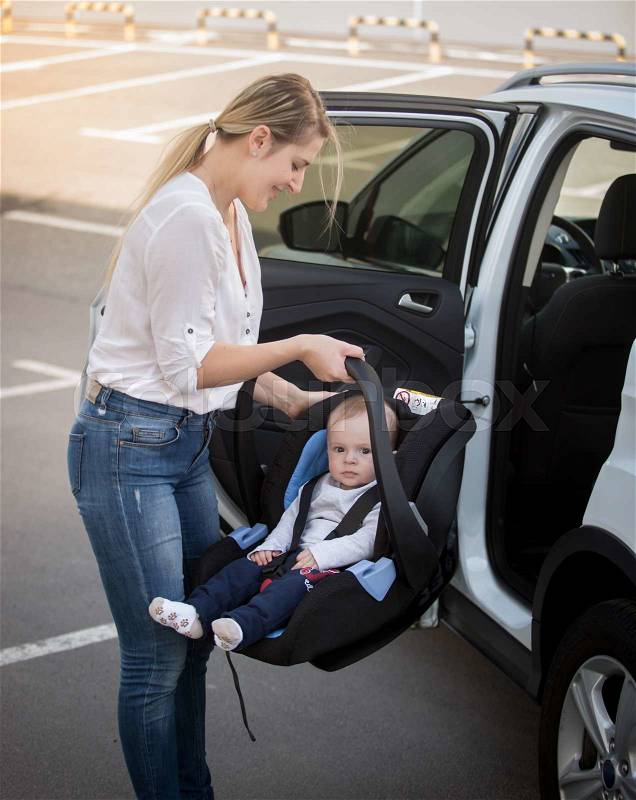 Portrait of young mother installing car child seat with baby, stock photo
