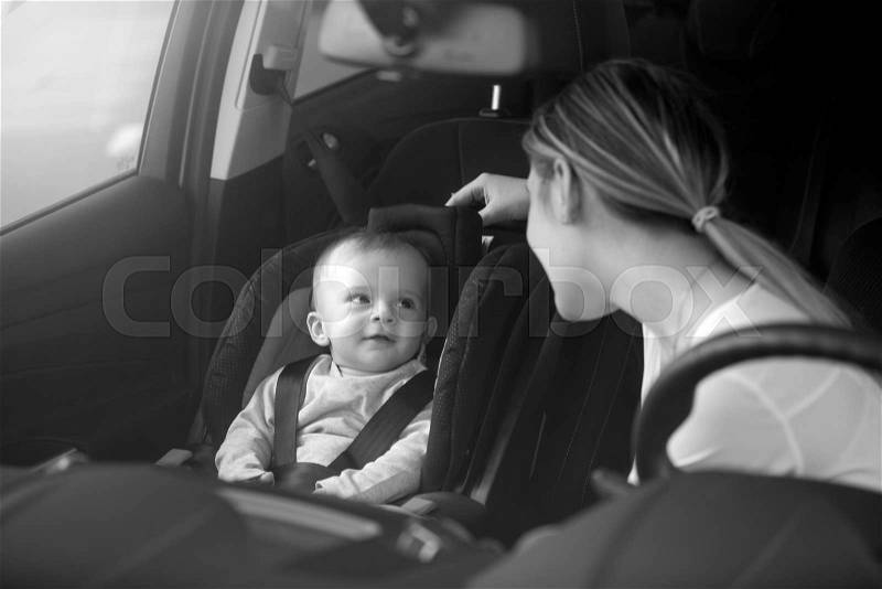 Black and white portrait of mother looking at baby sitting on car front seat, stock photo