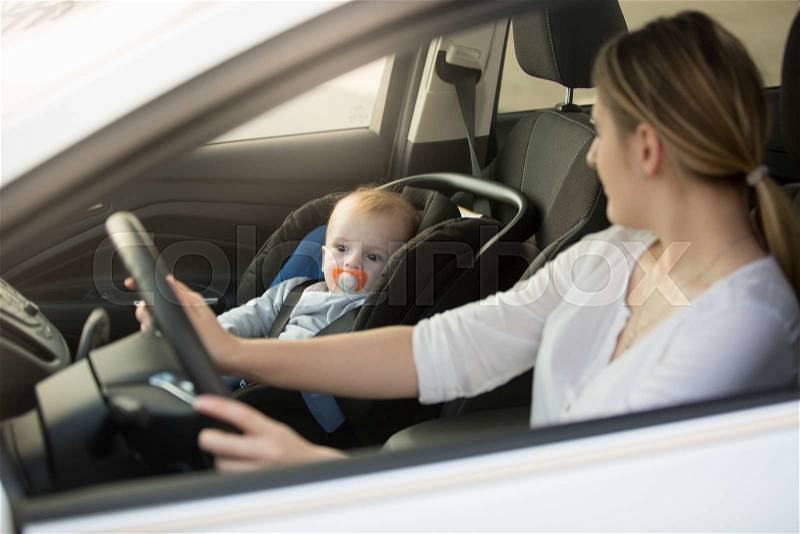 Portrait of woman driving car with baby sitting on front seat, stock photo