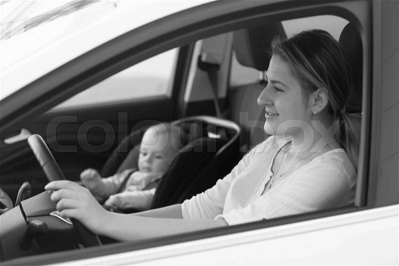 Black and white portrait of mother driving car with little baby boy sitting in safety seat, stock photo