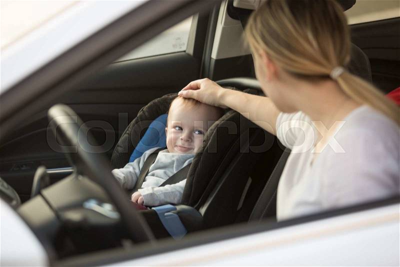 Young mother looking at baby boy sitting in car in baby seat, stock photo