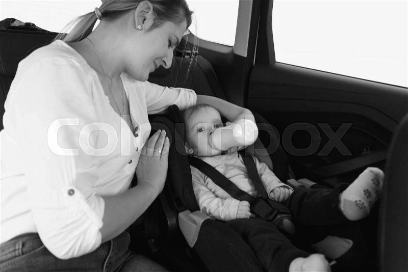 Black and white portrait of mother feeding baby in car safety seat, stock photo
