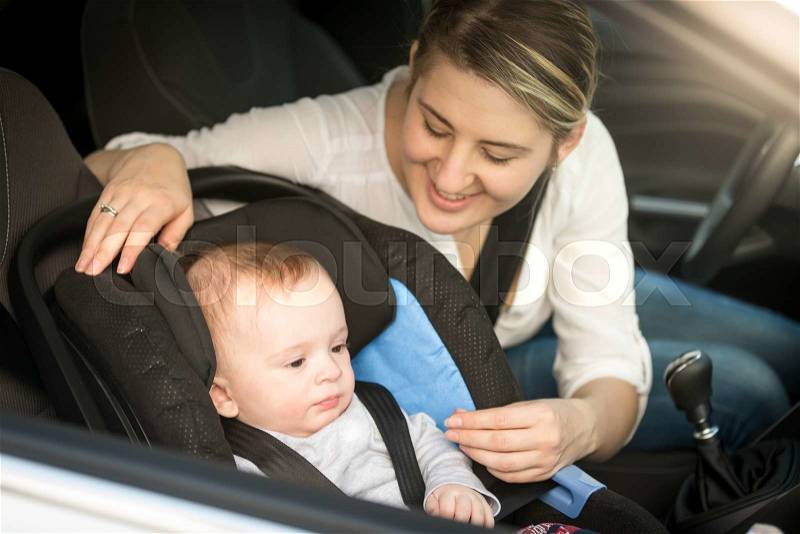 Portrait of smiling mother in car having her baby boy in safety seat, stock photo