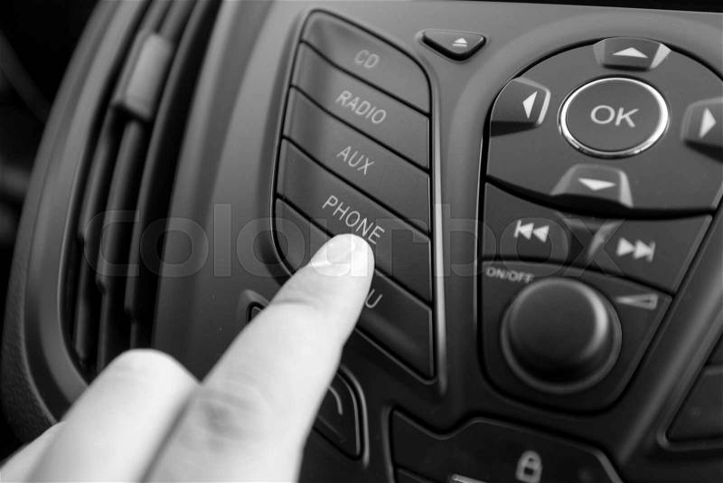 Black and white closeup photo of driver pushing radio button on dashboard, stock photo