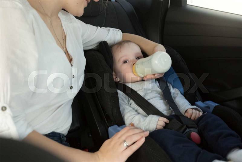 Portrait of mother giving her baby milk on car back seat, stock photo