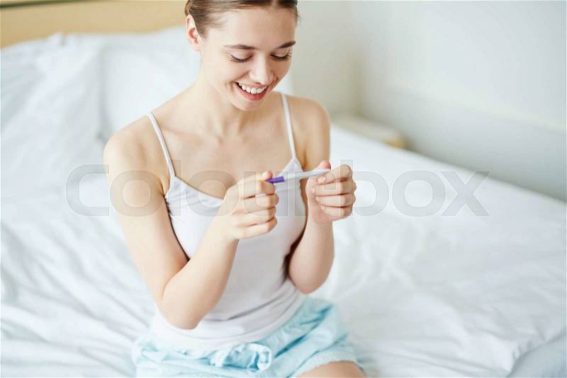 Happy young woman looking at positive pregnancy test, stock photo