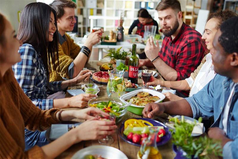 Group of happy friends sitting by table and having dinner, stock photo