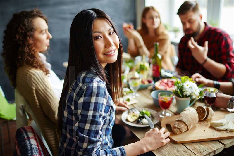 Pretty woman sitting at table with friends and having dinner, stock photo