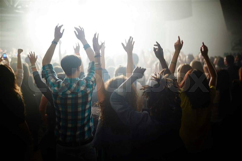 Crowd of ecstatic fans with raised hands dancing by songs of their favorite modern singer at live concert, stock photo