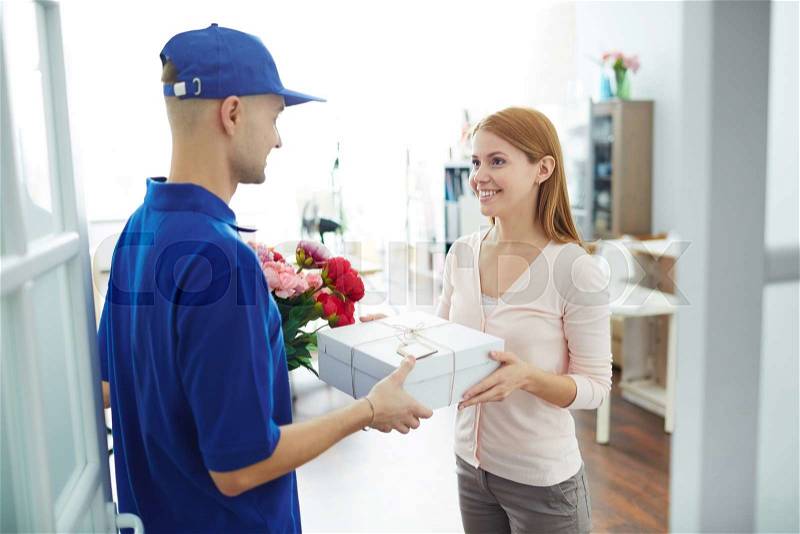 Young woman receiving gift-box and flowers from delivery man, stock photo